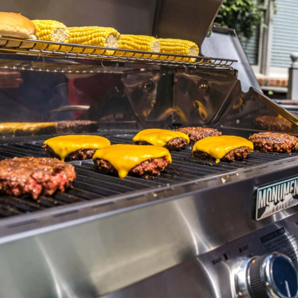 Grill with burgers and cheese, corn on the cob, and 'Monum' branding.