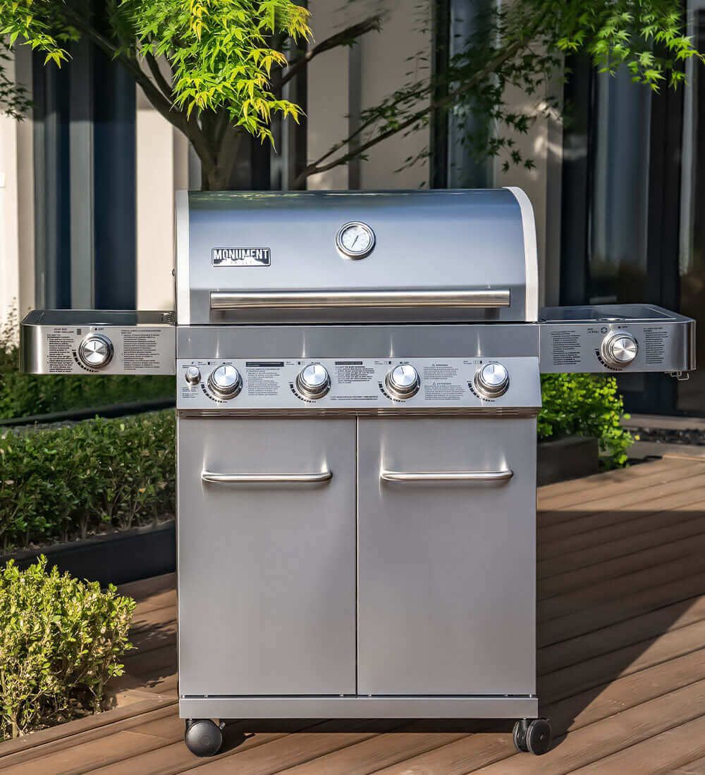 Stainless steel barbecue grill on a wooden deck with greenery in the background