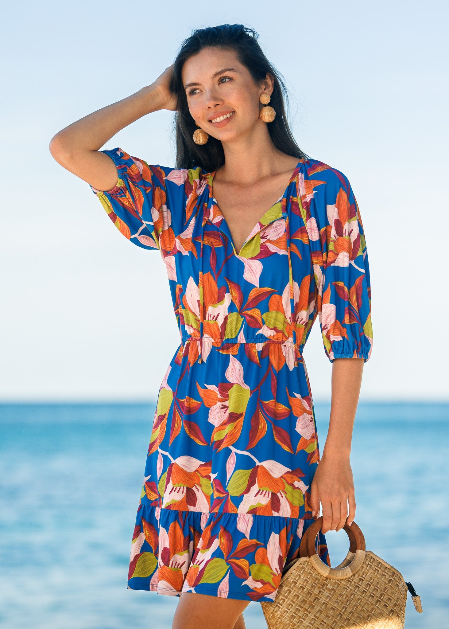 Woman wearing a colorful floral dress standing by the ocean.