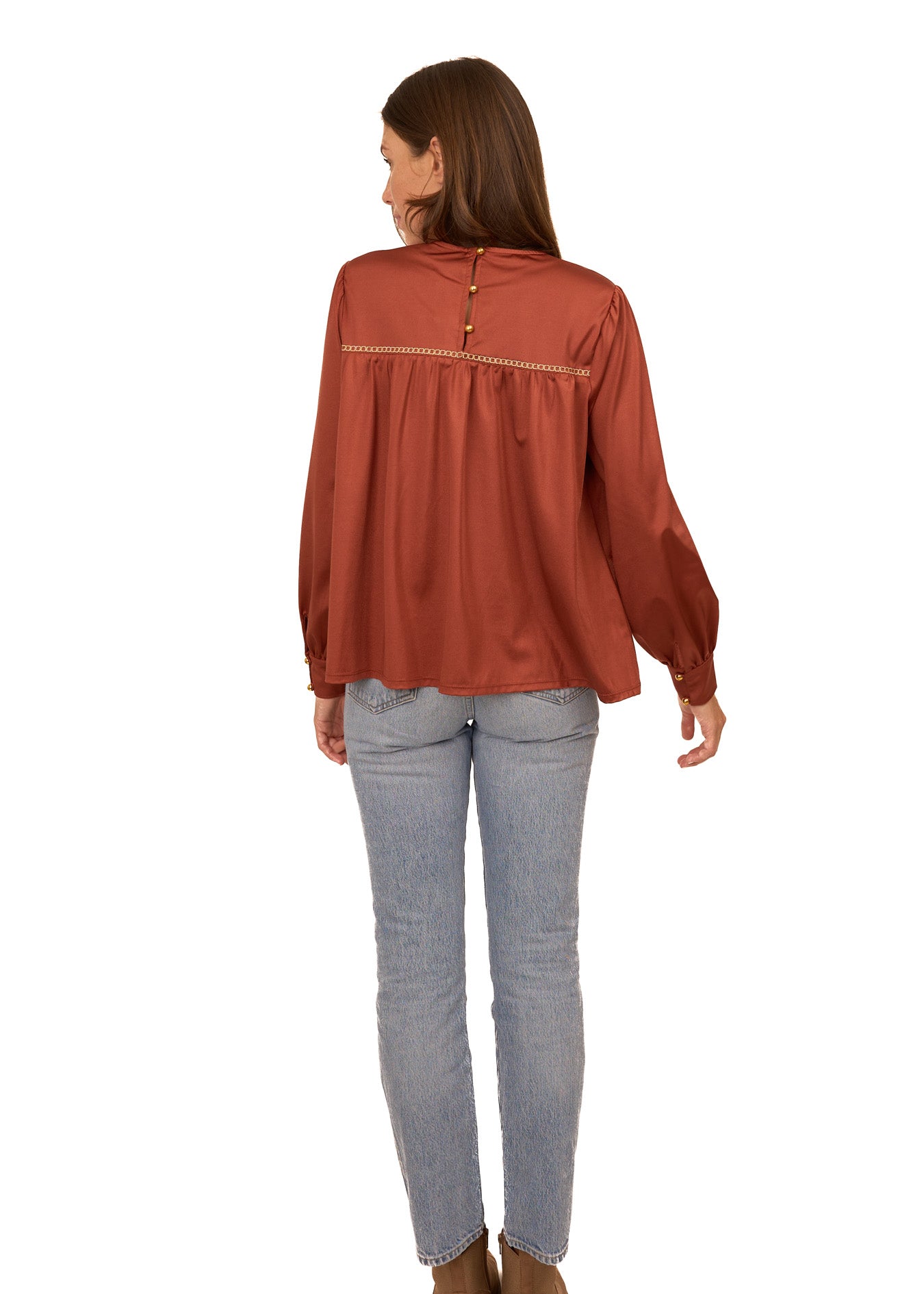Woman wearing a rust-colored blouse and light blue jeans on a white background
