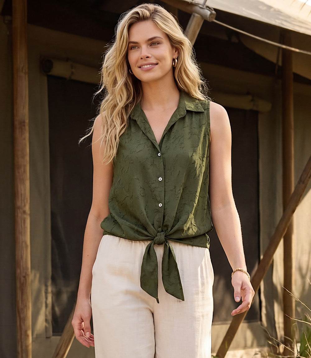 Woman wearing a green sleeveless shirt and beige pants standing in front of a wooden structure.