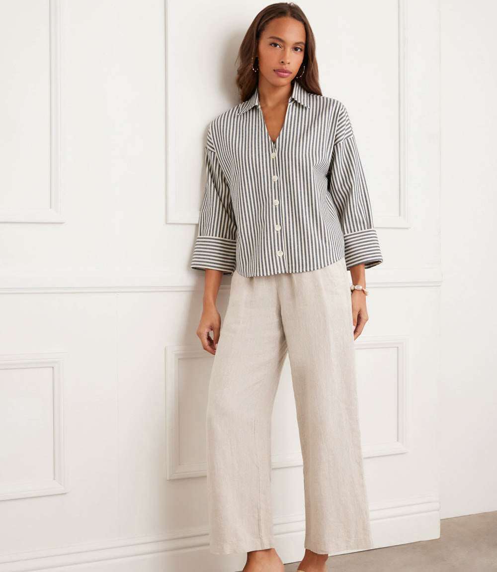 Woman wearing a striped shirt and wide-leg pants against a white paneled wall.