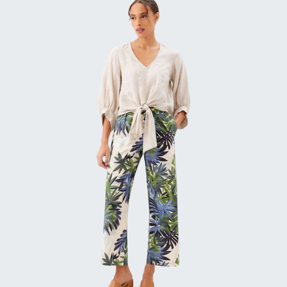 Woman wearing a beige top and tropical leaf pants on a white background