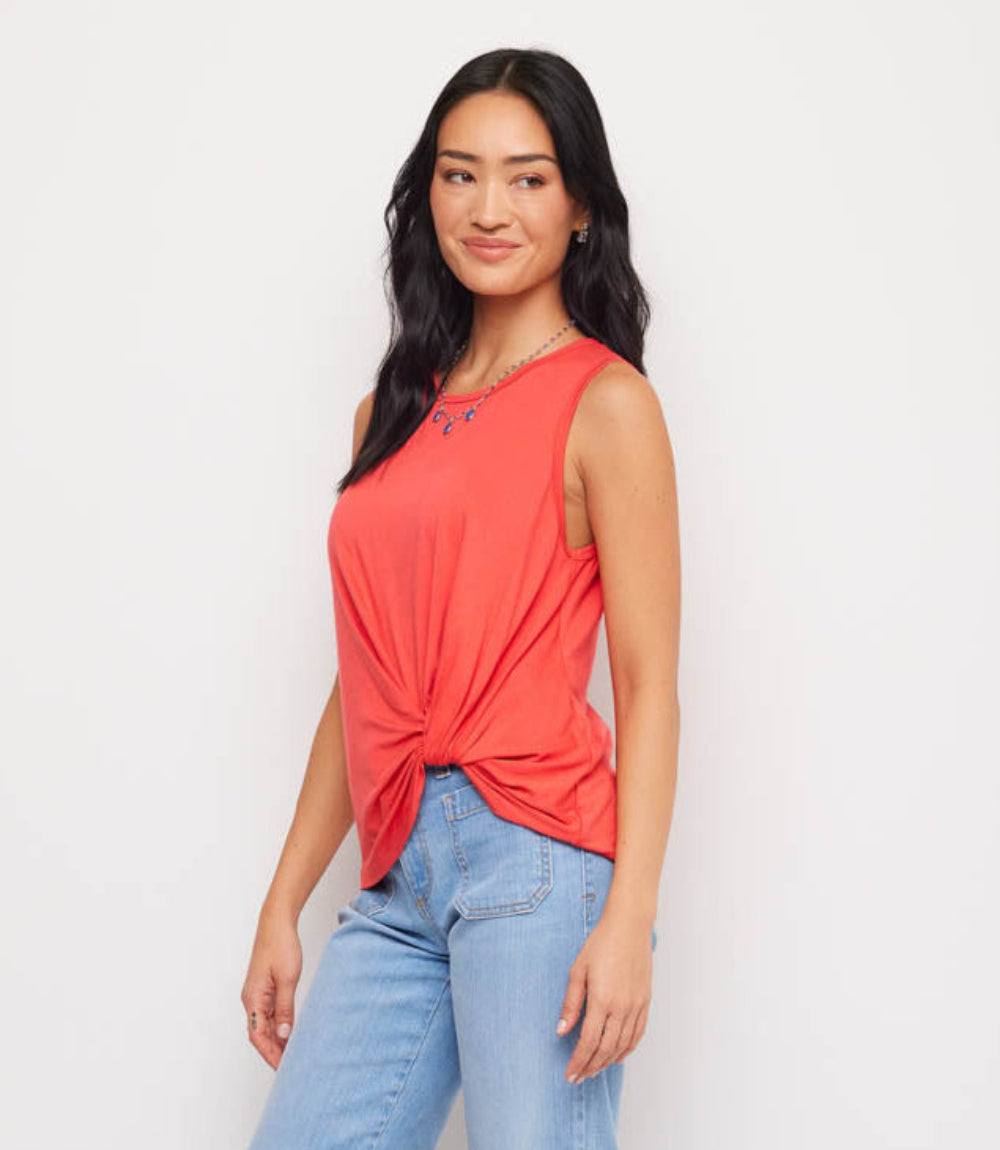 Woman wearing a coral tank top with a knot detail and light blue jeans on a white background
