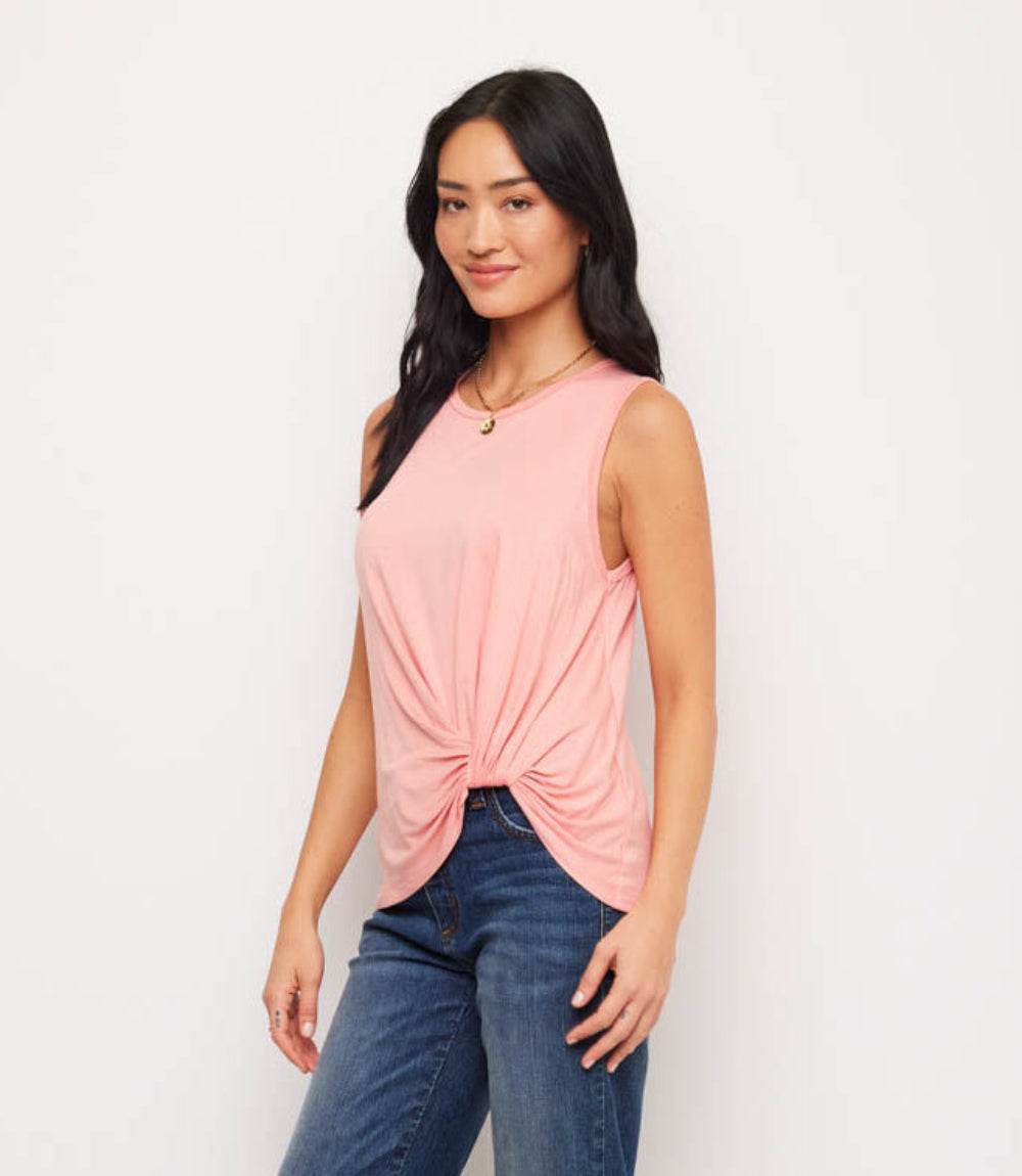 Woman wearing a pink sleeveless top with a knot detail and blue jeans on a white background