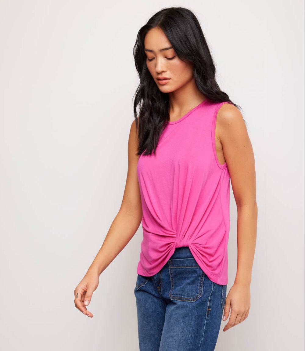 Woman wearing a pink sleeveless top with a knot detail and blue jeans on a plain background