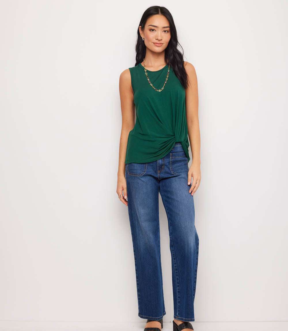 Woman wearing a green sleeveless top and blue jeans against a white background