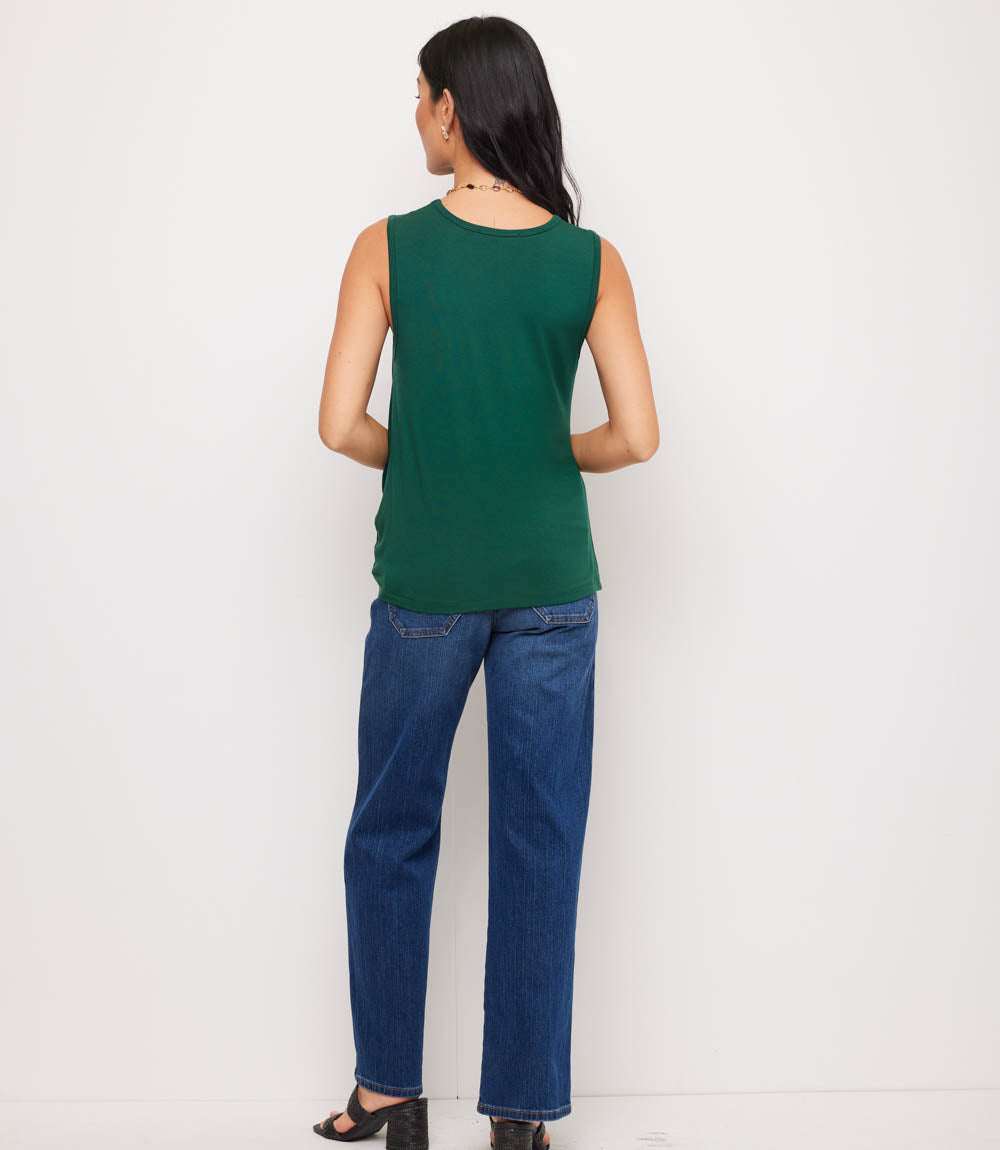A woman shown from the back wearing a sleeveless dark green top and blue jeans, standing against a plain white studio background.