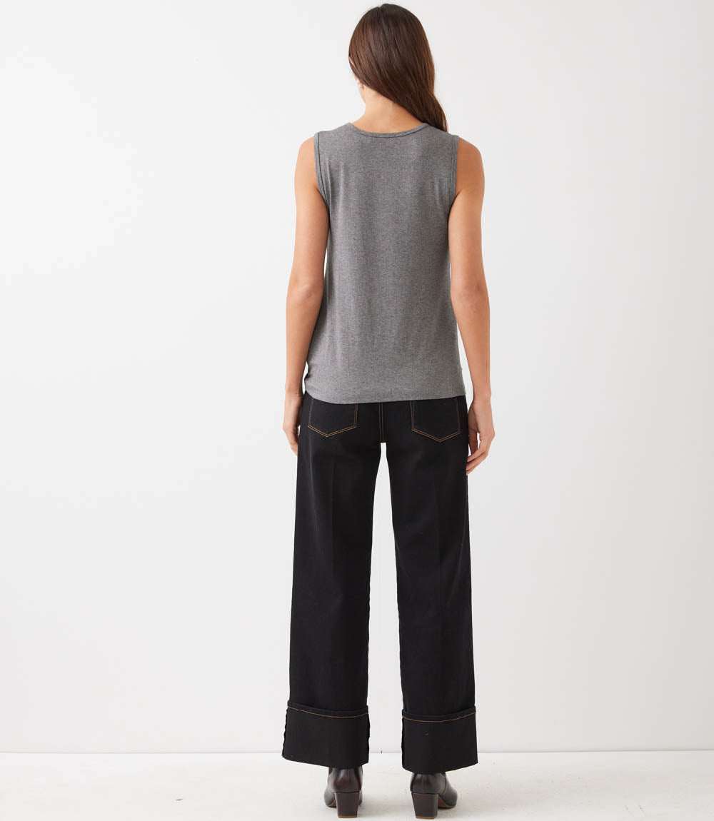A woman shown from the back wearing a gray sleeveless top and black wide-leg jeans with rolled hems, standing against a plain white studio background.
