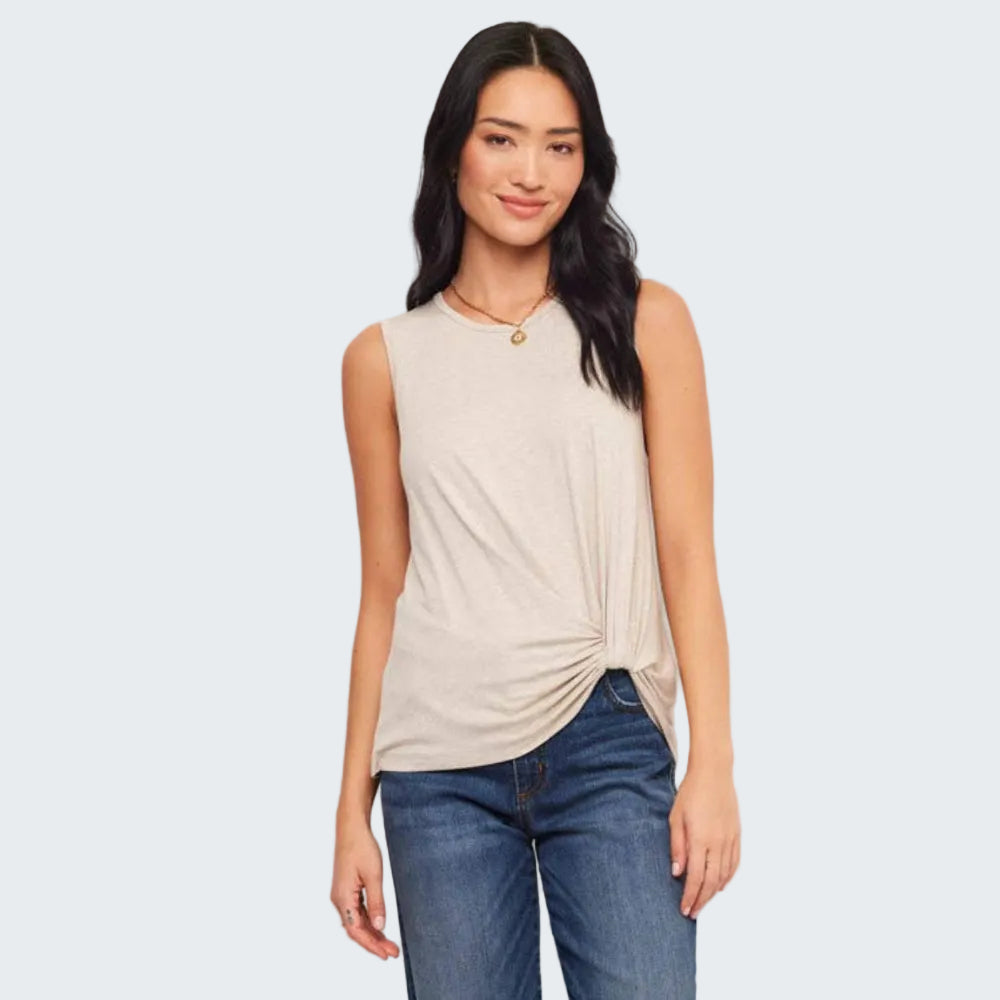 Woman wearing a beige sleeveless top and blue jeans against a white background