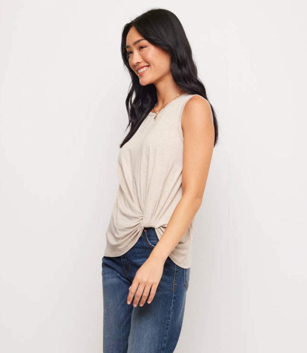 Woman wearing a beige sleeveless top and blue jeans on a white background