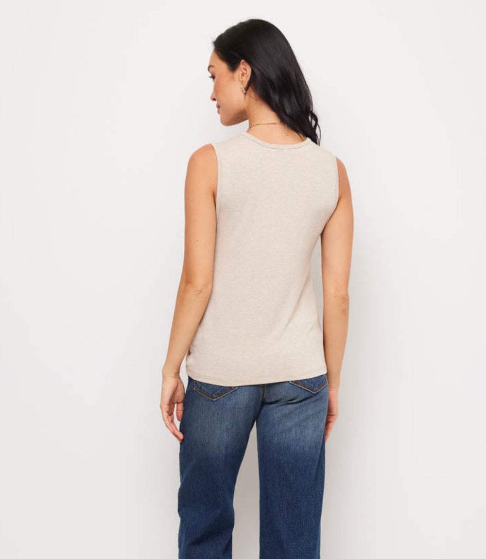 Woman wearing a beige sleeveless top and blue jeans on a white background