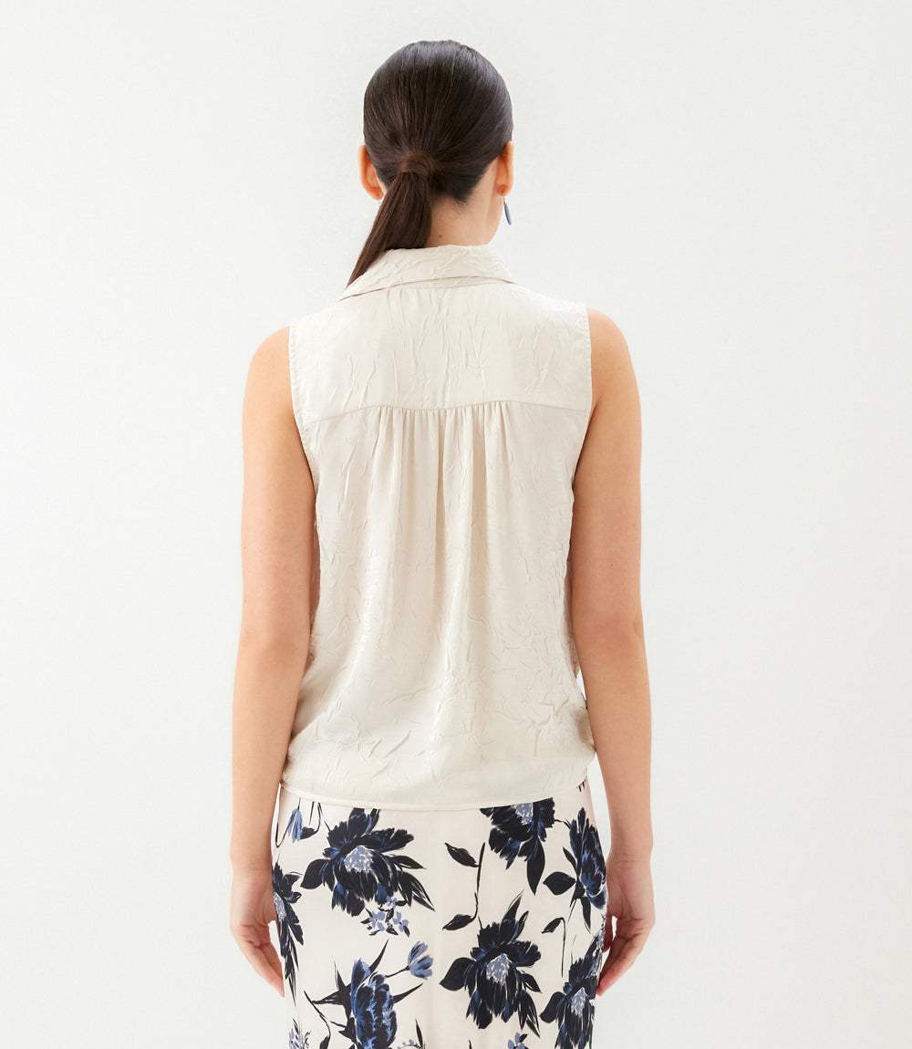 Person wearing a sleeveless beige top and floral skirt on a white background
