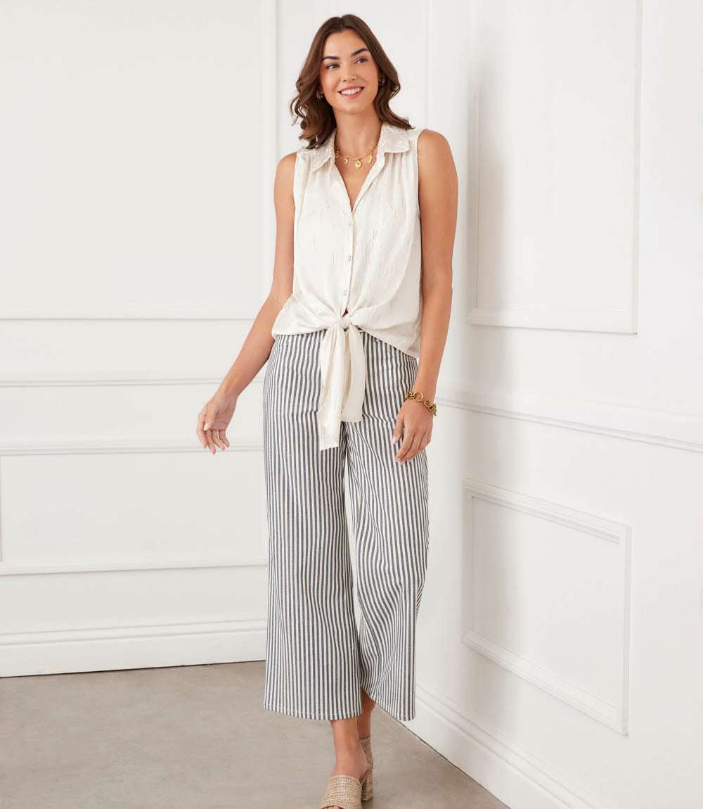 Woman wearing a white sleeveless top and striped pants against a white wall.