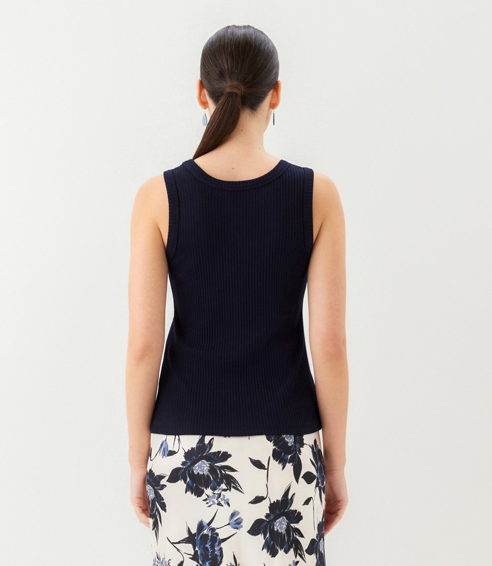 Woman wearing a black sleeveless top and floral skirt against a white background