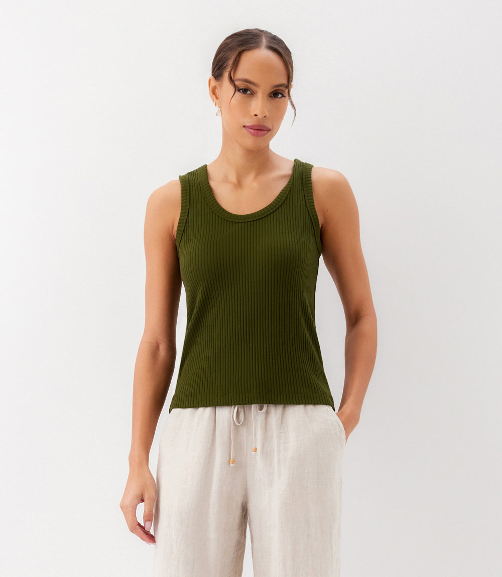 Woman wearing a green ribbed tank top and white pants on a light gray background