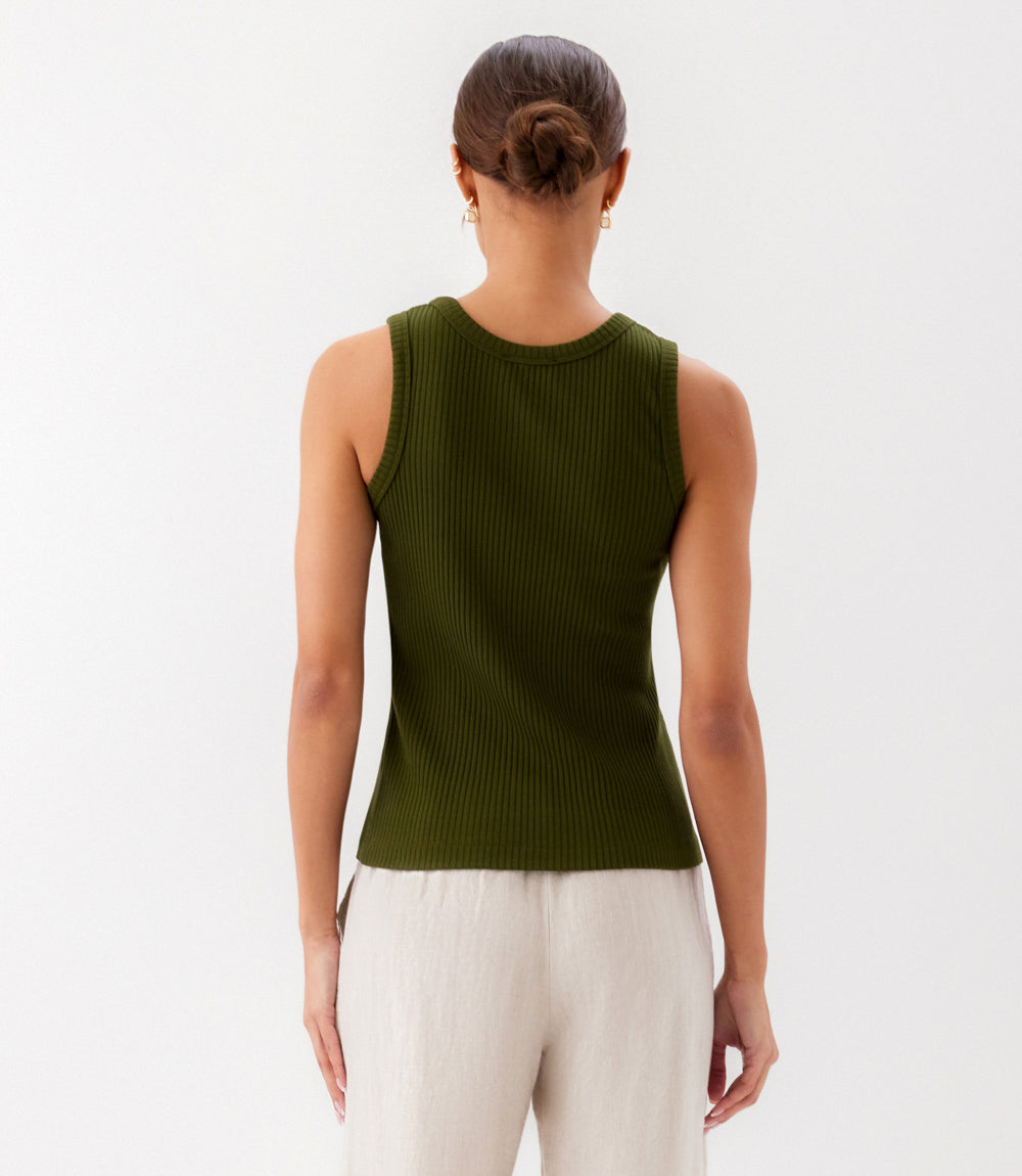 Person wearing a green ribbed tank top and white pants on a light gray background