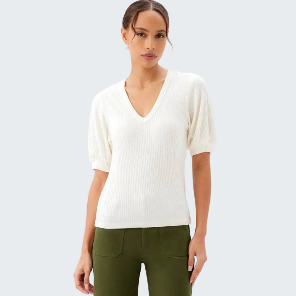 Woman wearing a white sweater and green pants on a plain background