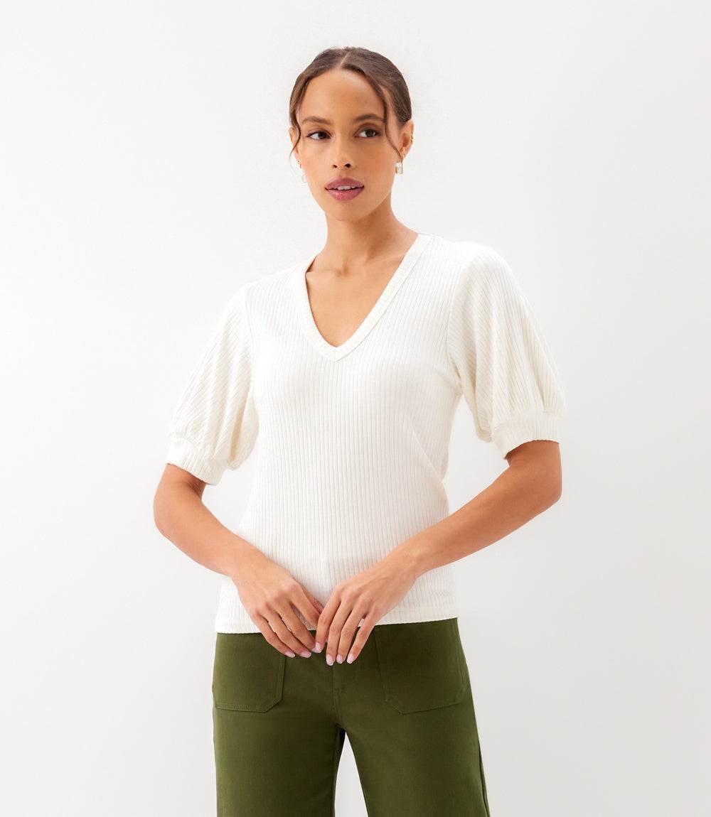 Woman wearing a white ribbed sweater and green pants on a white background