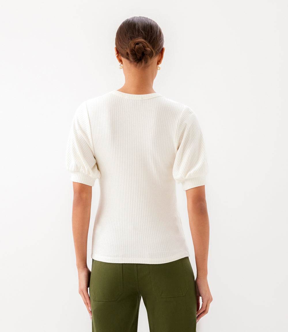 Person wearing a white sweater and green pants on a light gray background