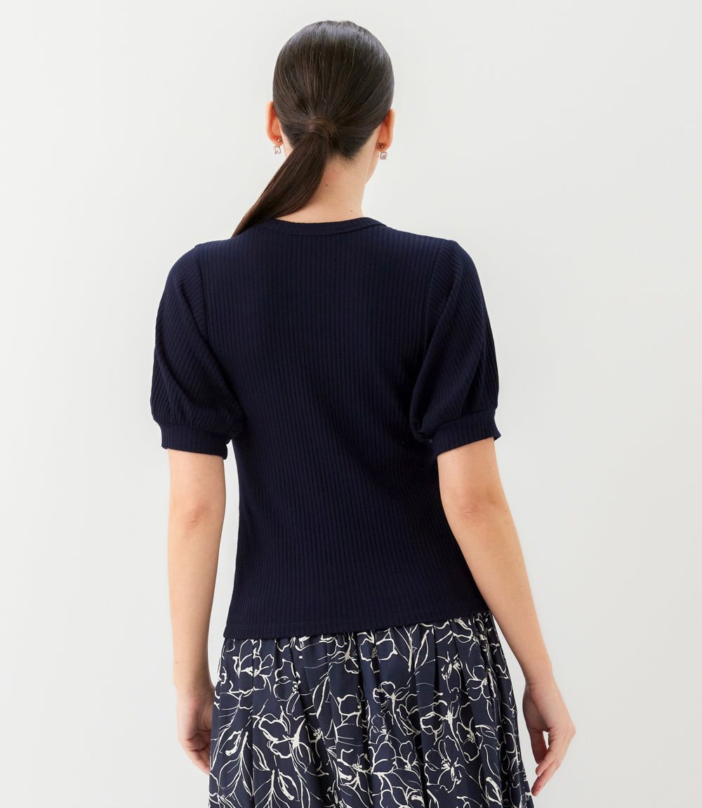 Person wearing a navy blue sweater with puffed sleeves and a floral skirt on a plain background