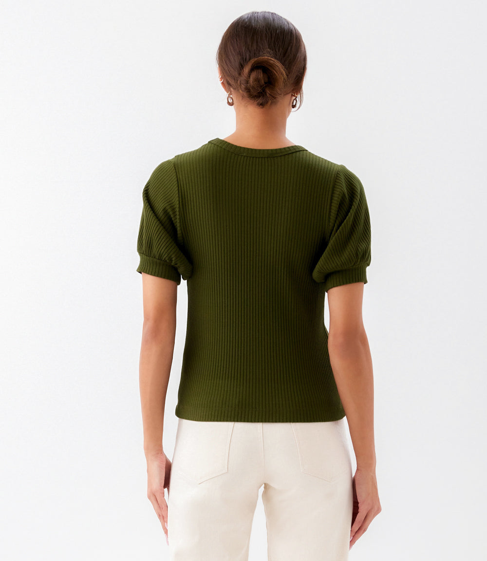 Person wearing a green ribbed sweater and white pants on a light gray background