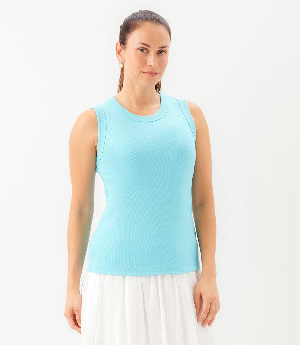 A woman modeling a light blue sleeveless crewneck tank top paired with a white skirt, photographed against a clean white studio background.