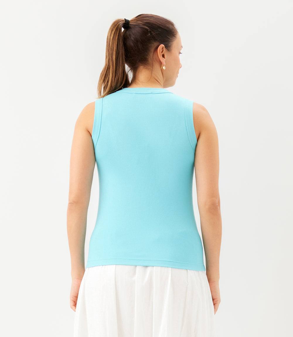 Woman wearing a light blue sleeveless top and white skirt on a plain background