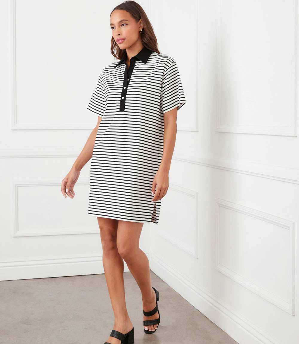 Woman wearing a black and white striped dress with a black collar against a white wall.