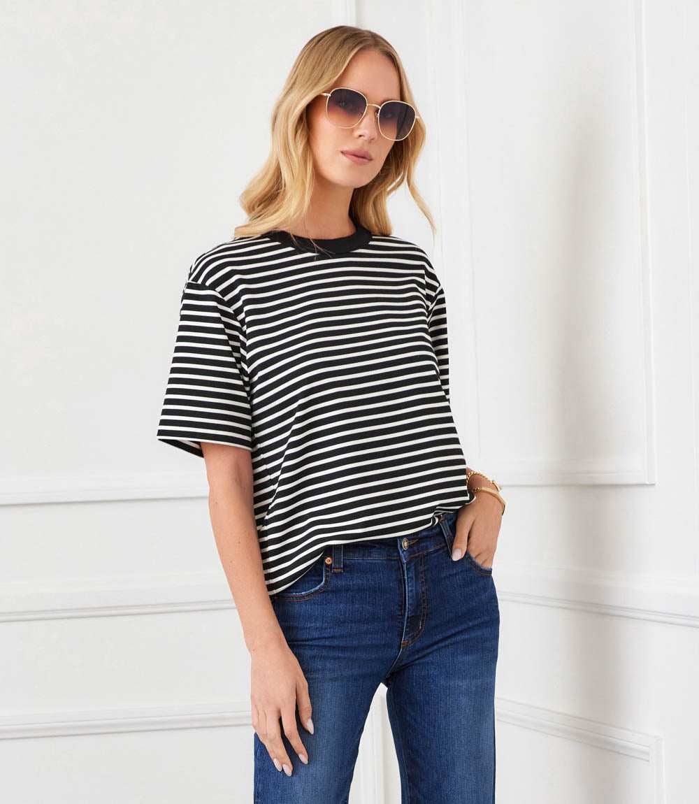Woman wearing a black and white striped shirt and blue jeans against a white background