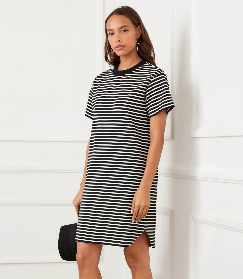 Woman wearing a black and white striped dress against a white wall.