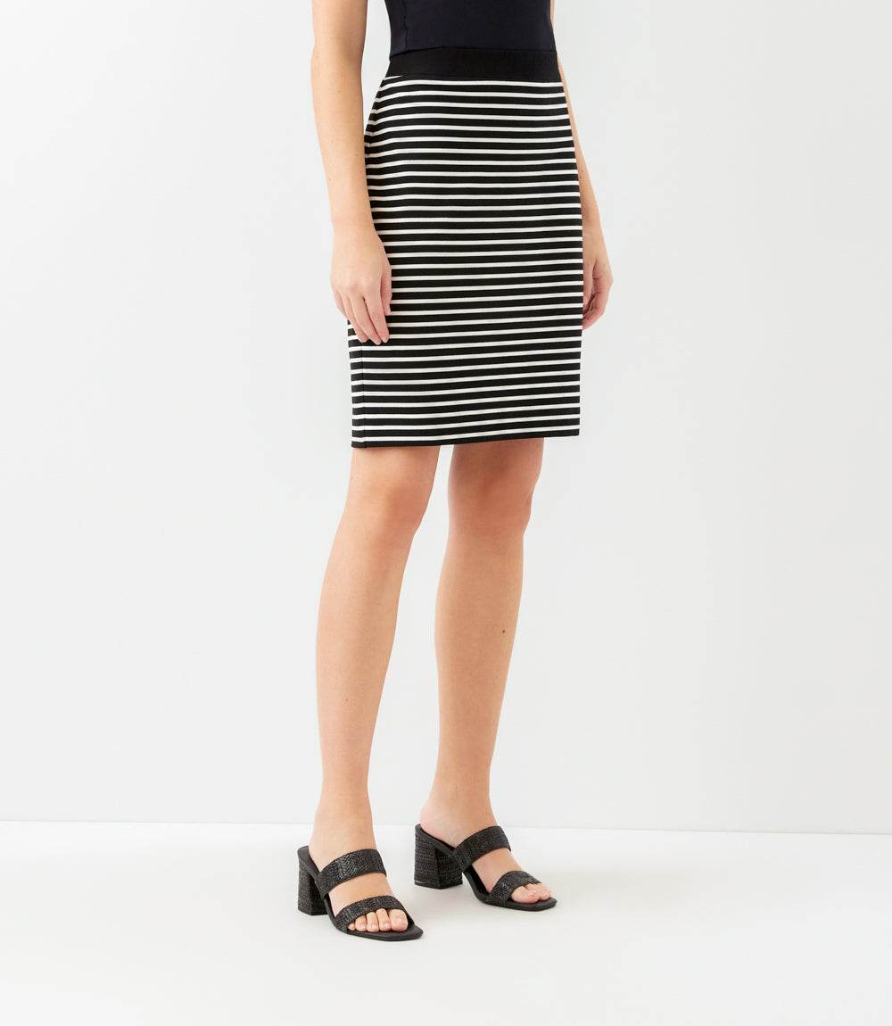 A model wearing a black and white horizontally striped pencil skirt with a black top and black block-strap heeled sandals, shown from the waist down against a plain white studio background.
