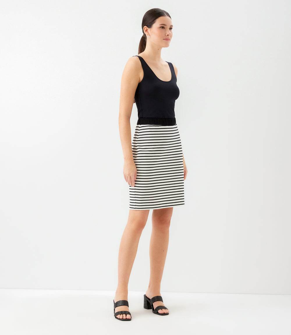A woman modeling a sleeveless black scoop-neck top and a black and white horizontally striped knee-length skirt, paired with black heeled sandals, against a plain white studio background.