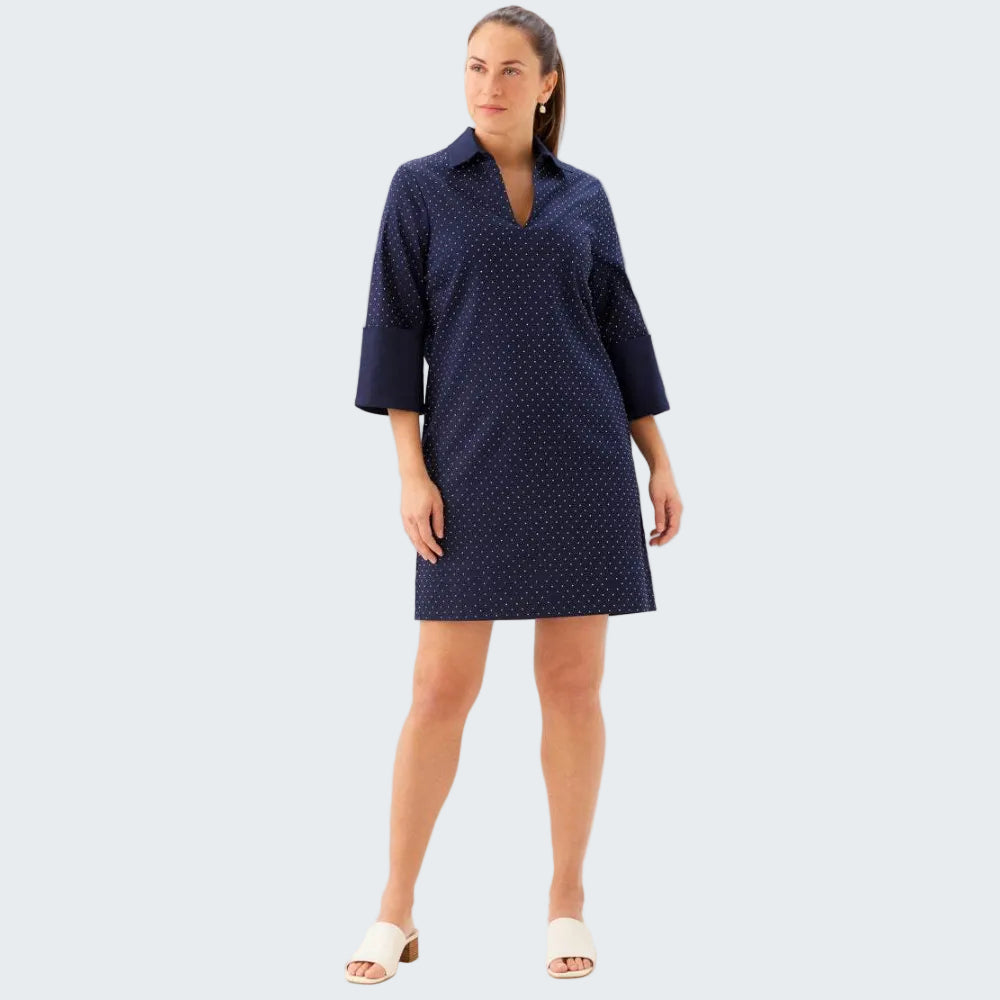 A woman modeling a navy blue collared shirt dress with a small white polka dot pattern, styled with white slide sandals against a plain white studio background.