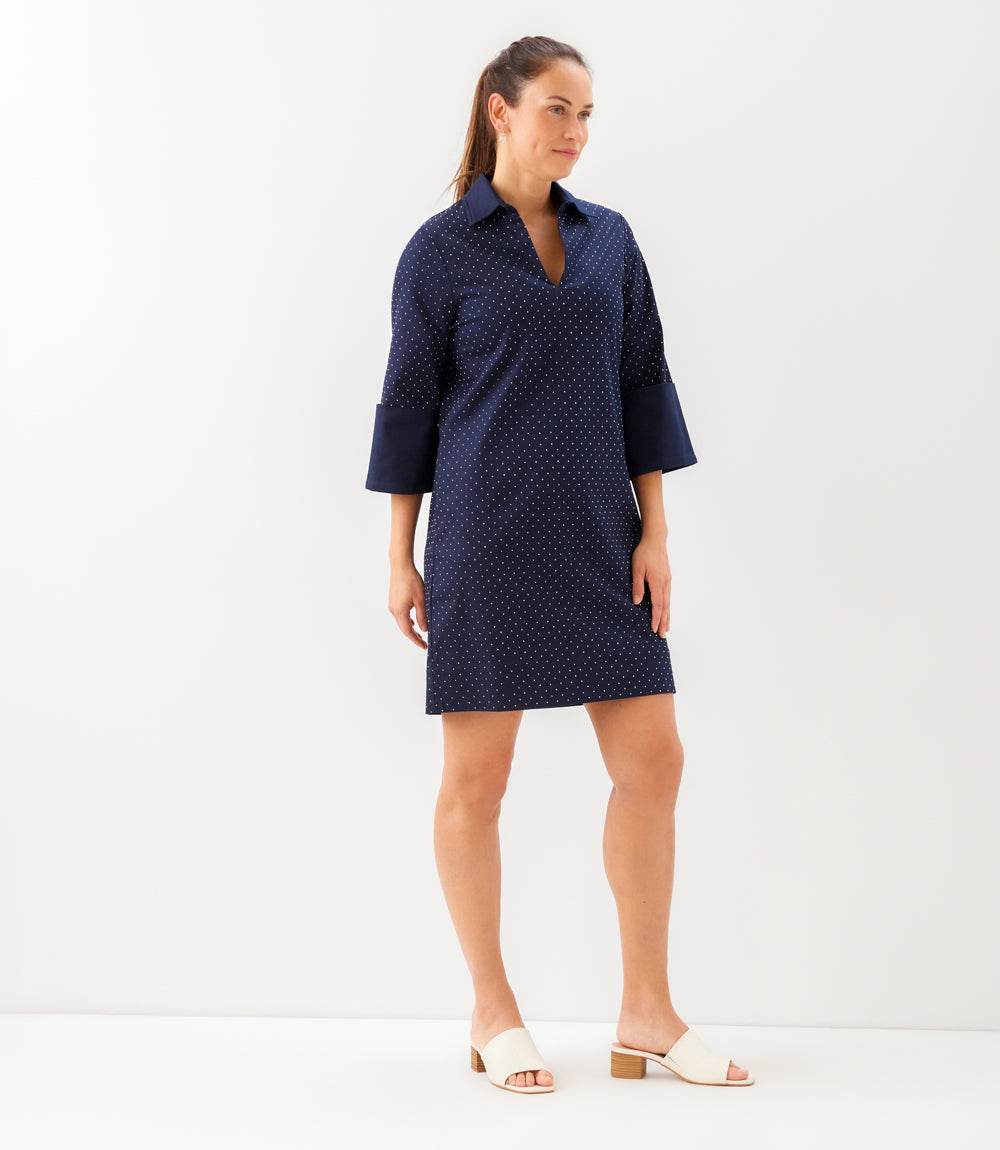Woman wearing a navy blue dress with white polka dots on a white background