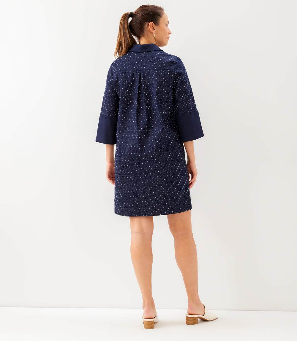 A woman wearing a navy blue mini shirt dress with a small white polka dot pattern, shown from the back against a plain white studio background.