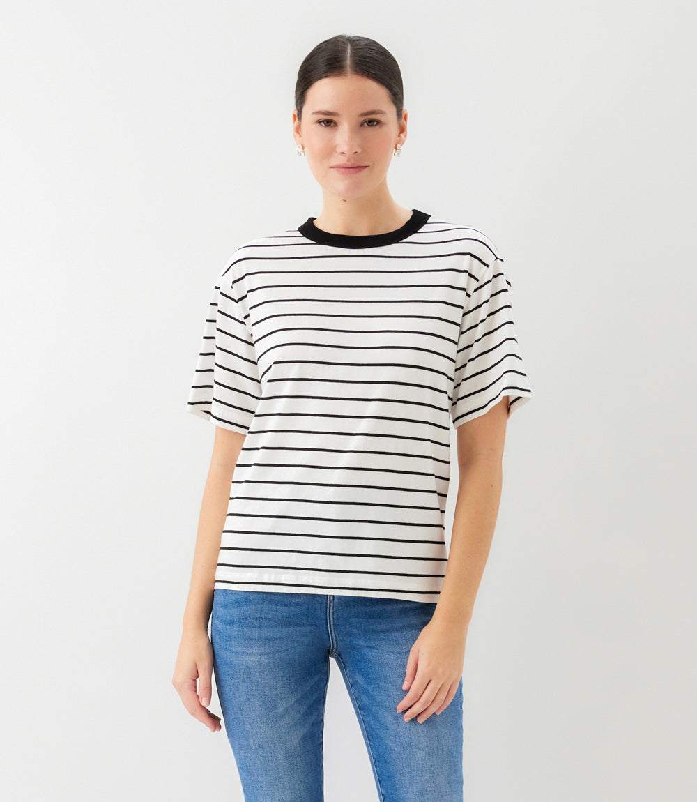 Woman wearing a black and white striped shirt with blue jeans on a light gray background
