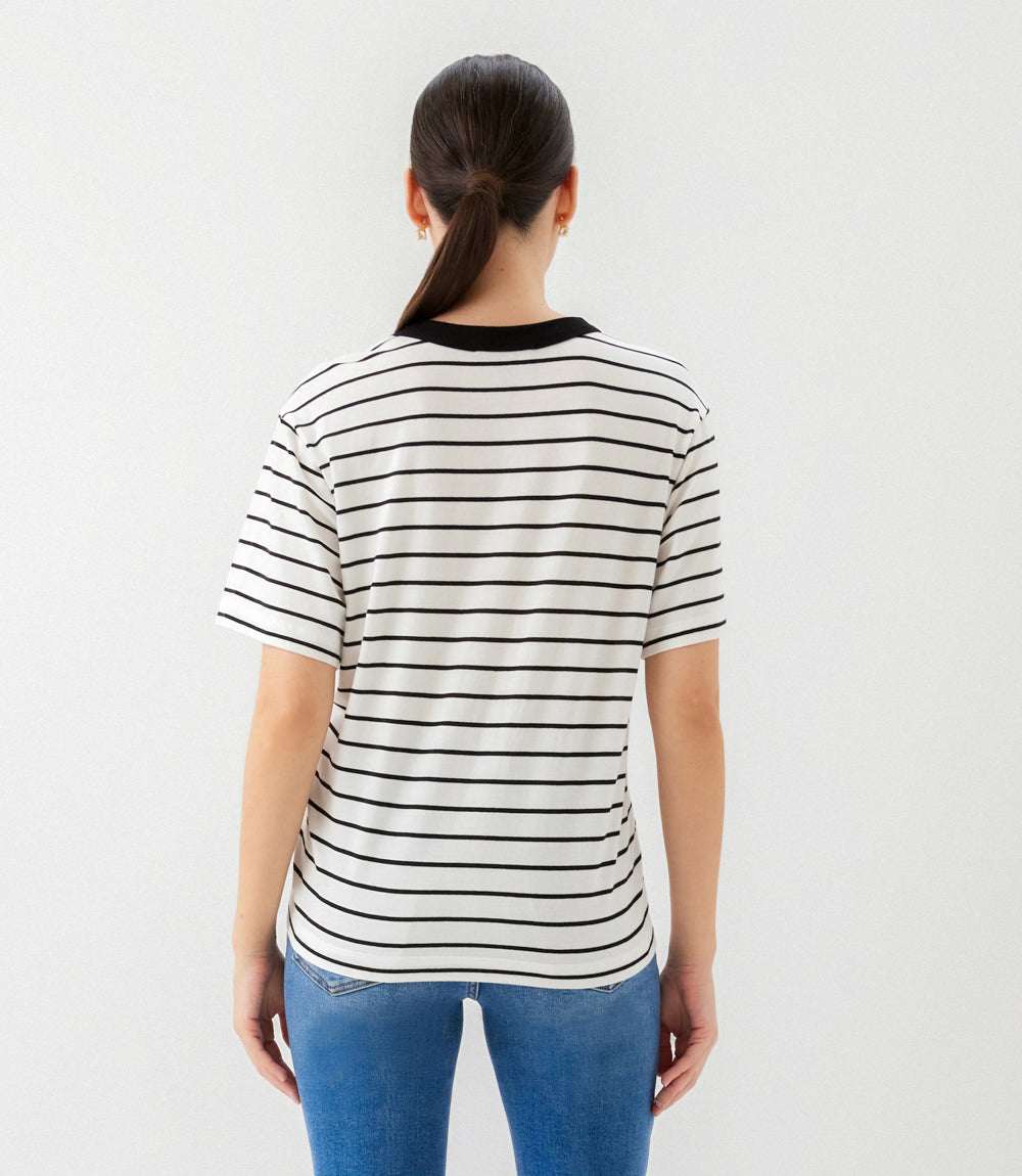 A woman viewed from behind wearing a short-sleeve striped t-shirt with black horizontal stripes on a white base and a black crew neck, paired with blue jeans against a plain white background.