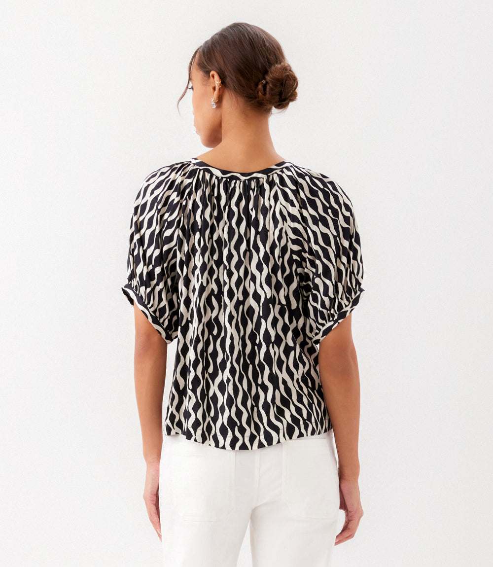 Woman wearing a black and white patterned blouse against a white background