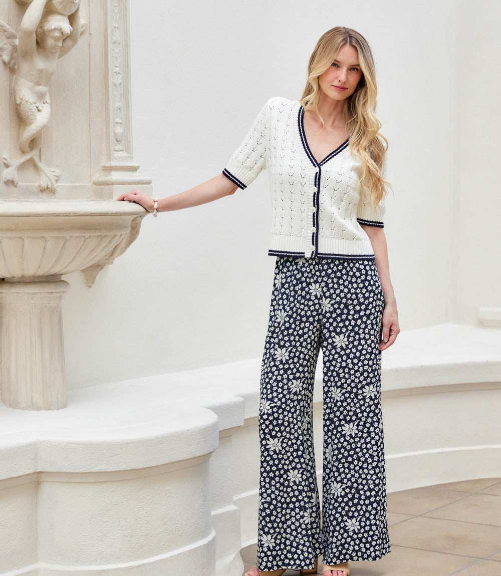 Woman in a white cardigan and black and white patterned pants standing in an elegant interior setting.