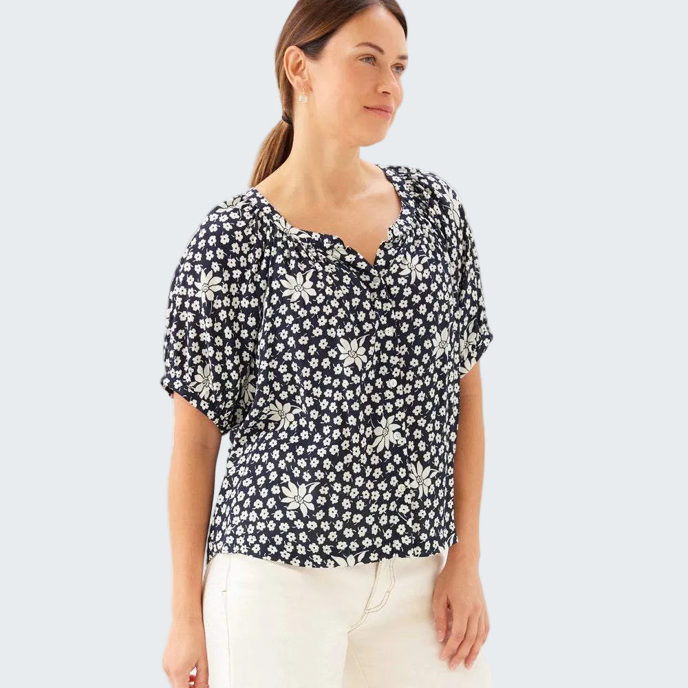 Woman wearing a black floral blouse with white pants on a white background