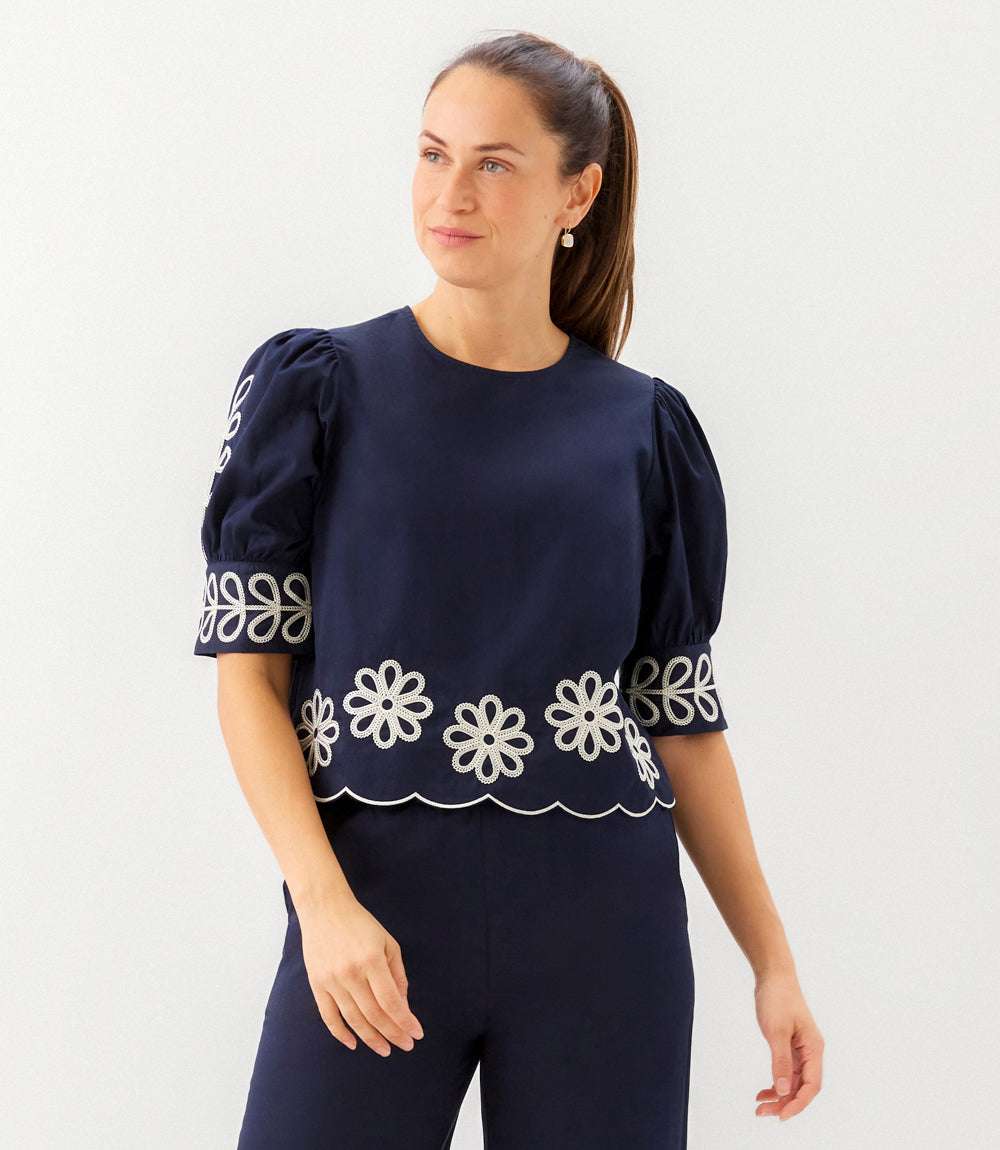Woman wearing a navy blue top with white floral patterns on a plain background