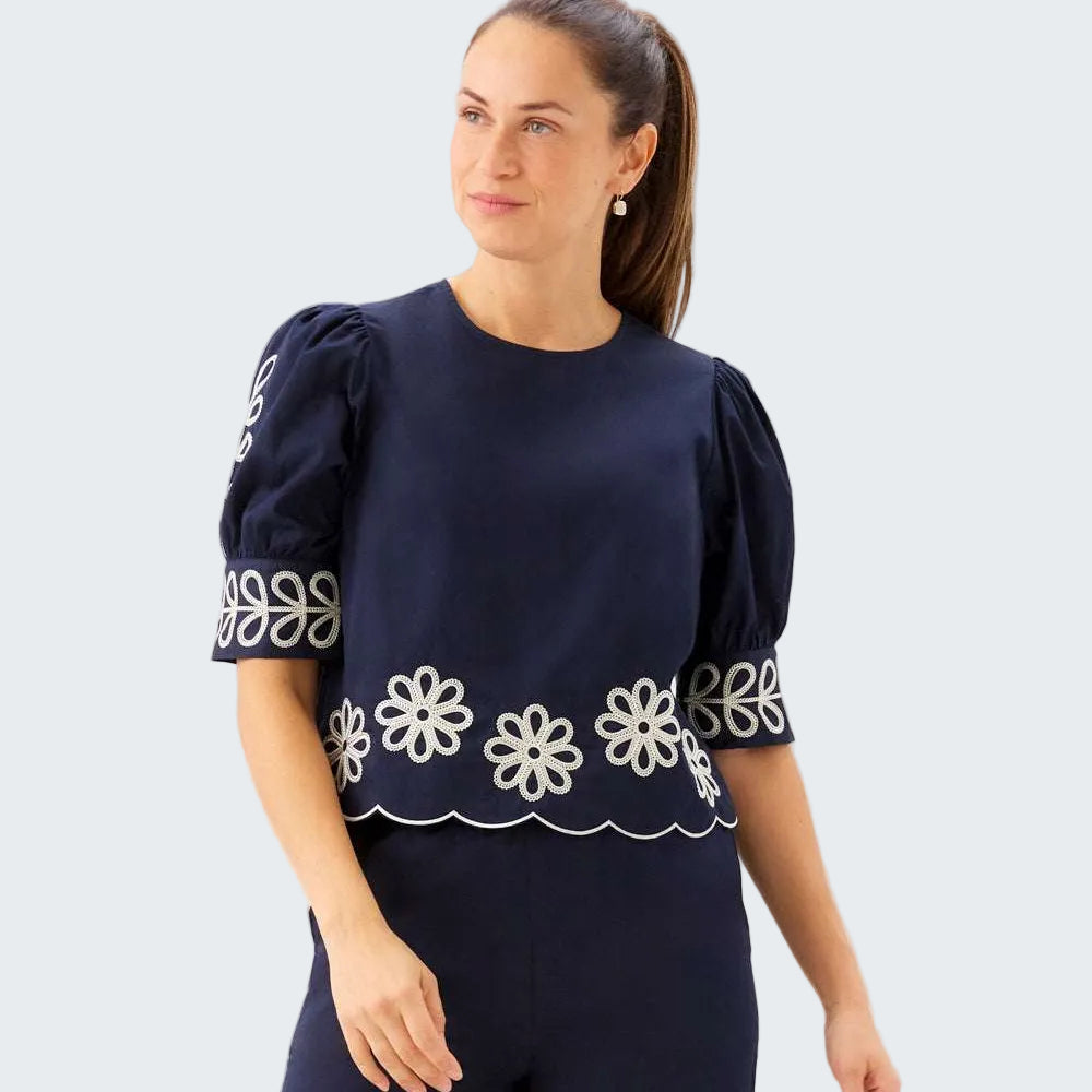Woman wearing a navy blue top with white floral patterns on a plain background