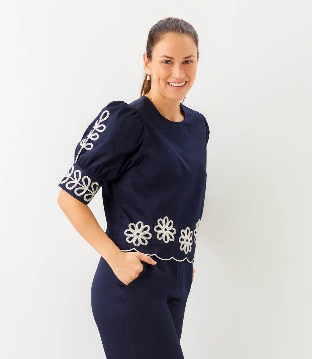 Woman wearing a navy outfit with white floral patterns on a plain background