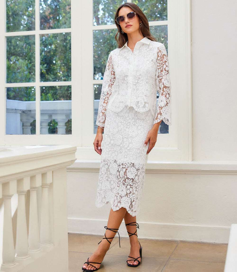 Woman wearing a white lace dress standing in a bright room with large windows.