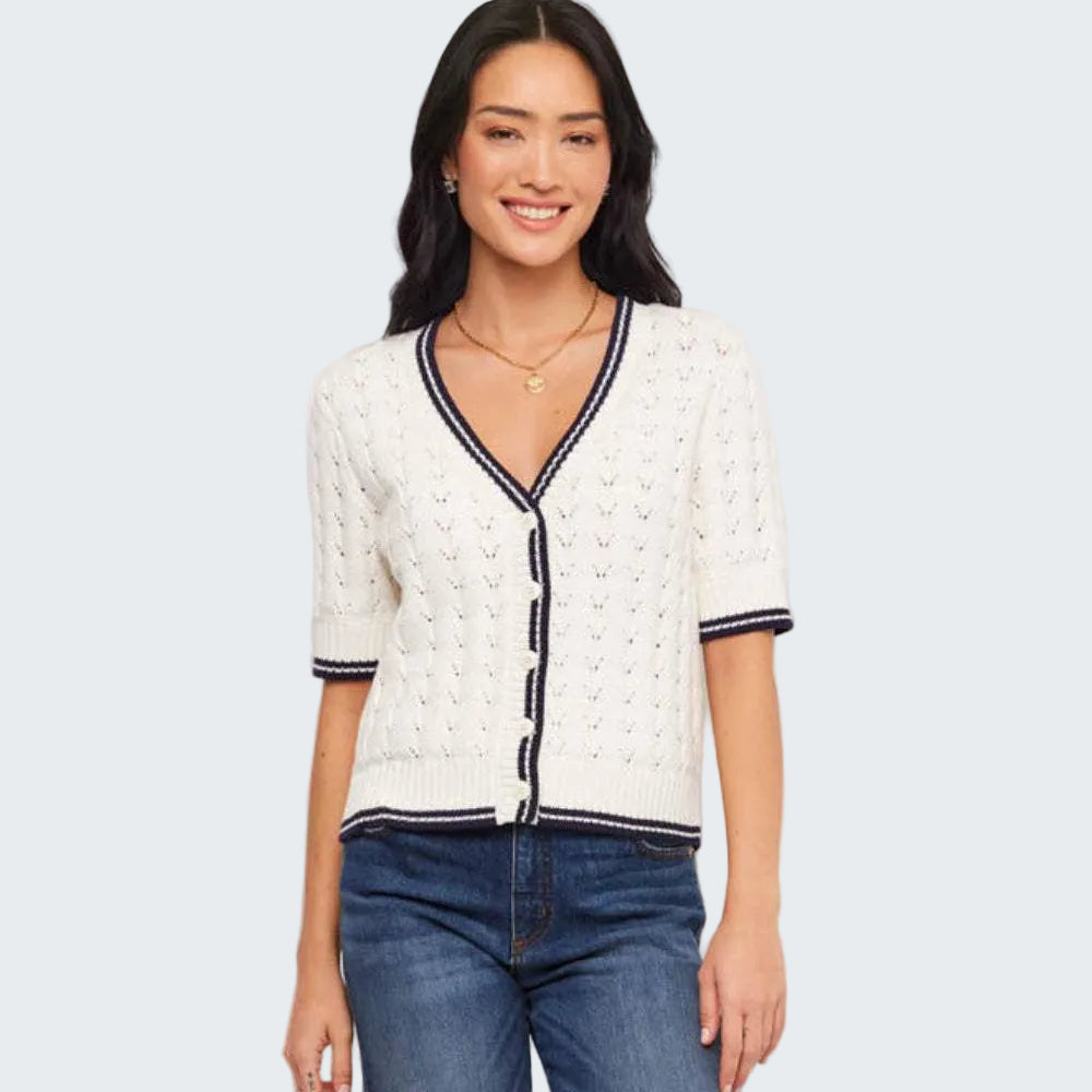 Woman wearing a white cardigan with black trim and blue jeans on a light gray background