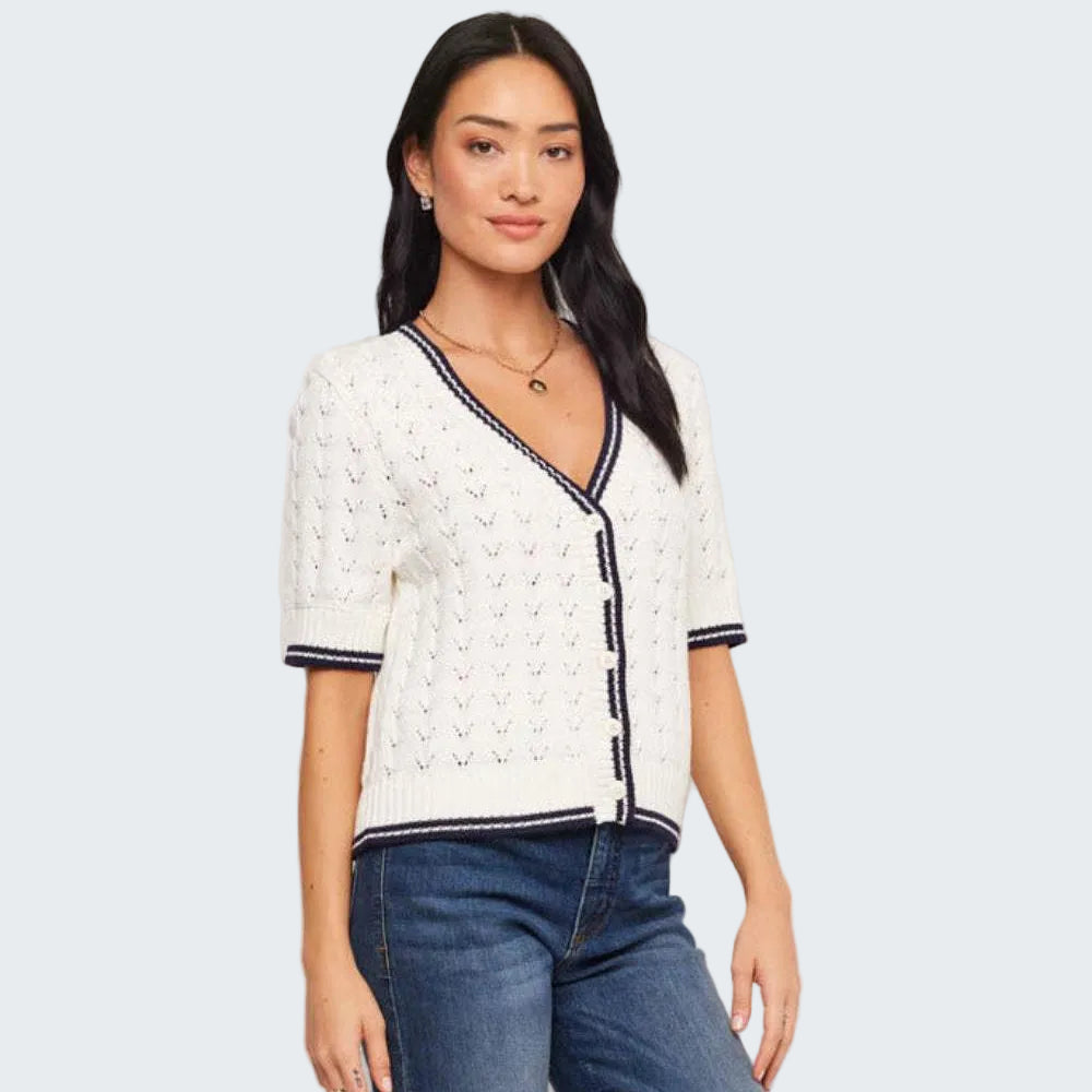 Woman wearing a white cardigan with navy trim and blue jeans on a plain background