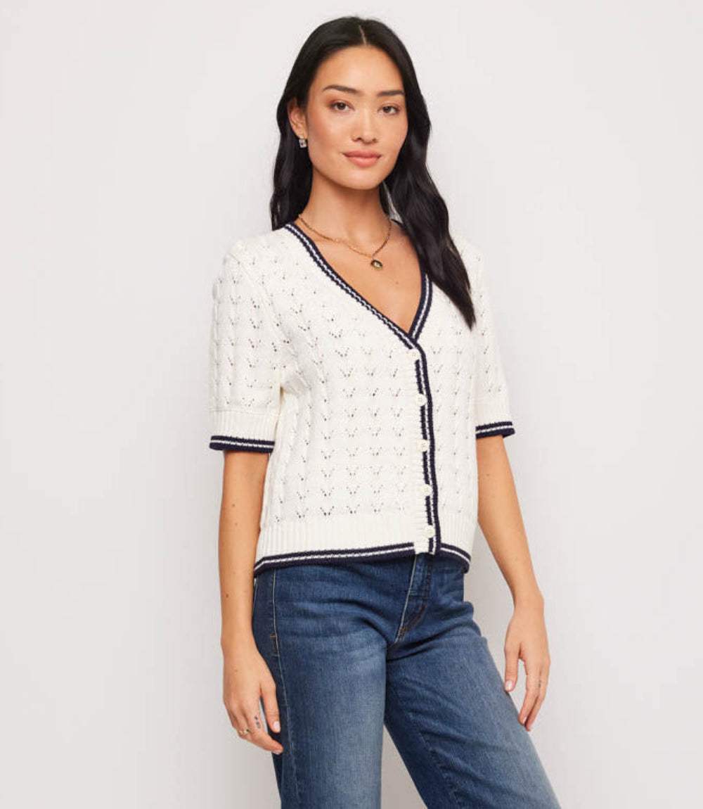 Woman wearing a white textured top with black trim and blue jeans on a plain background