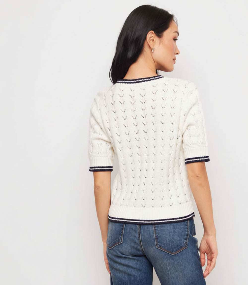 Woman wearing a white cable knit sweater with black trim on a plain background