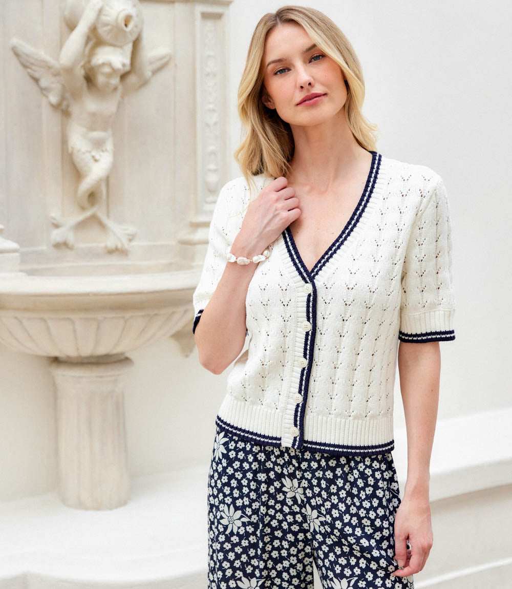 Woman wearing a white cardigan with navy trim in an elegant indoor setting.
